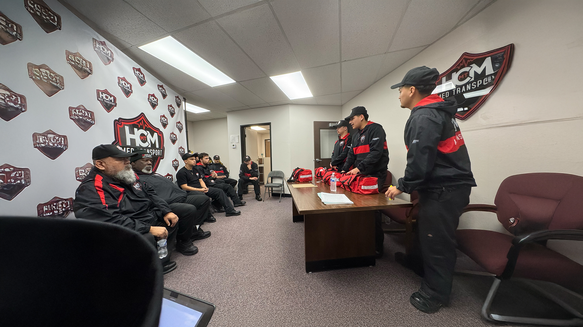 Crew seated in the HCM office during a shift briefing led by a supervisor.