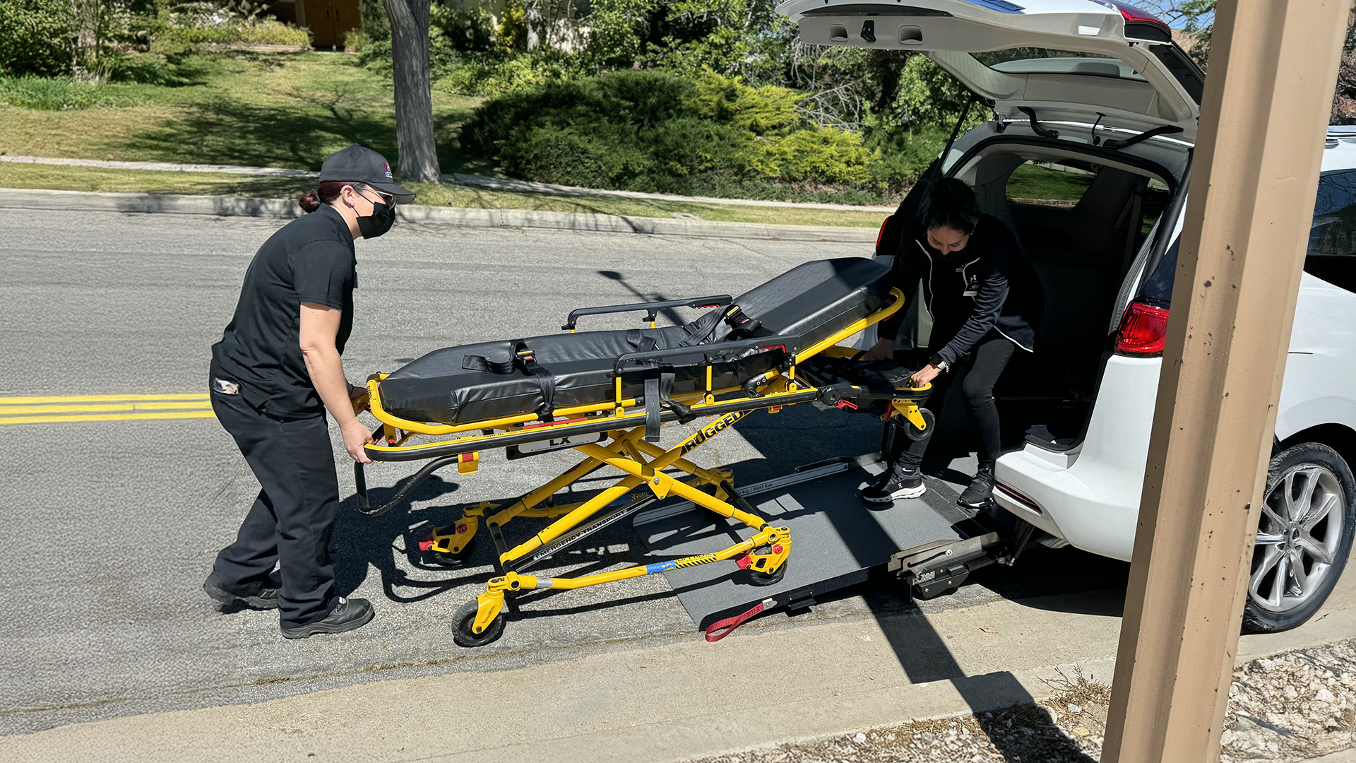 Two crew members loading a gurney into the back of an HCM transport vehicle.